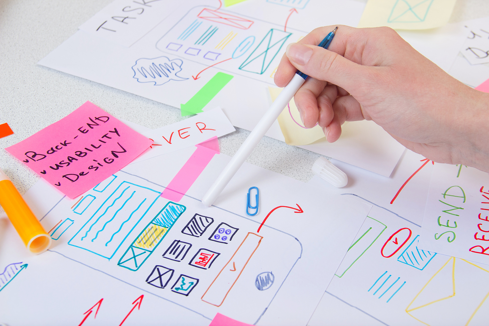 デスクに広げたWebサイト制作の設計図（ワイヤーフレーム）を指差して検討する手元の写真。Webに詳しくない担当者でも取り組める集客の基本ステップを表現。