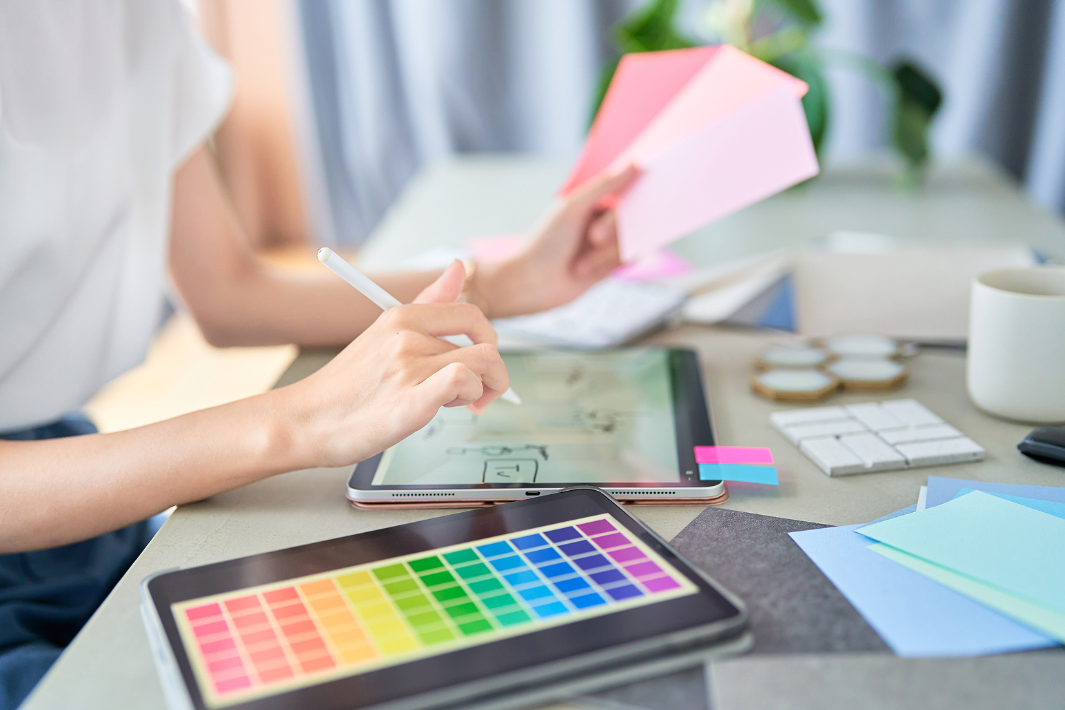タブレット端末を使ってWebサイトのデザインを制作する女性の手元。スマートフォン対応を重視したレスポンシブなWebサイト制作をイメージ。